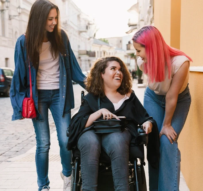 Friends with disabled woman on wheelchair walking together on sidewalk