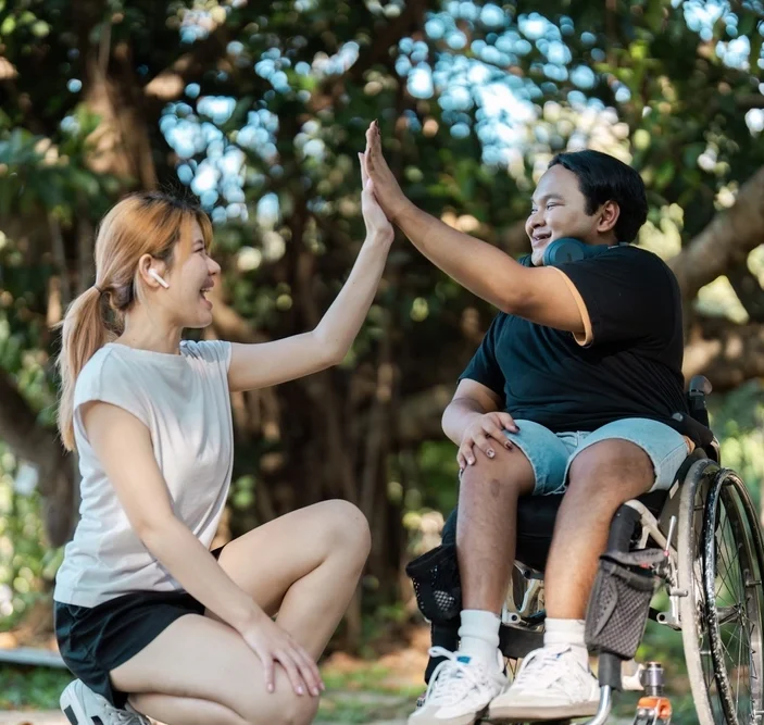 Disabled person on wheelchair high five a nurse in park