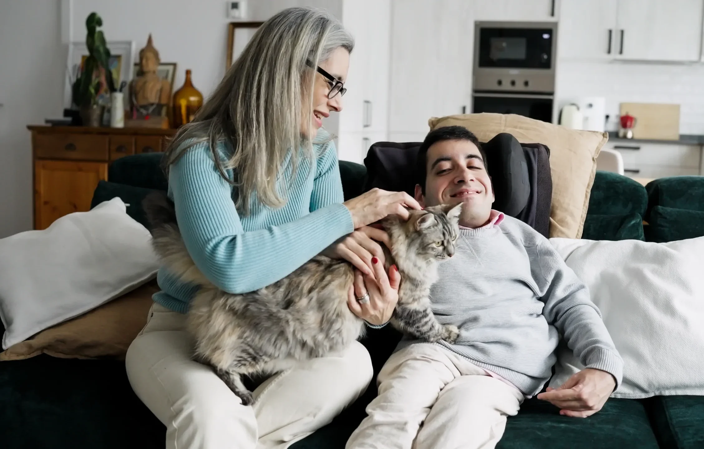 Mother petting a cat with disabled son sitting on sofa