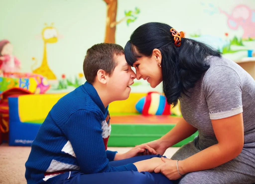 Down syndrome disabled young kid in class, playing with teacher